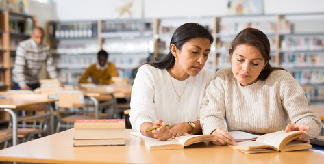 Two young adult women gaining new skills at public library, reading books and making notes