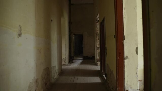 Moving forward along narrow corridor of old scary abandoned and destroyed building, stabilized camera, POV. Passage to old dusty spiral wooden staircase with broken railings, climb up steps.