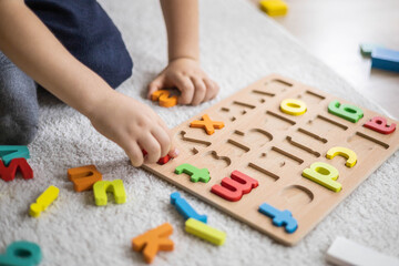 Obraz na płótnie Canvas Male kid playing with wooden eco friendly alphabet letters board on table top view intellectual game