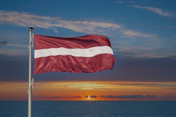 Fototapeta premium State flag of the Republic of Latvia against the backdrop of sunrise.
