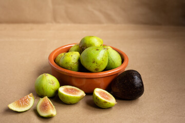 A bowl of figs and cut pieces on a light brown background