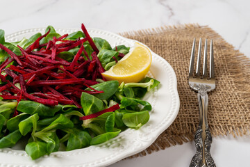 Slimming salad of lambs lettuce leaves and raw beet. Green corn salad and grated raw beet on a white plate and fork over marble surface. Vitamin vegetable salad closeup. Vegan low calories diet.