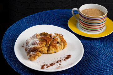 Mini sweet brioches topped with cinnamon powder and grated coconut on a dish and a mug of latte for a breakfast. Selective focus.