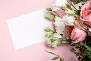 Holiday greeting card mockup with flowers on light pink background, top view, flat lay. White wedding invitation mockup and floral decor