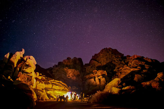 A group by a campfire that lights up granite rocks under a starlit sky.