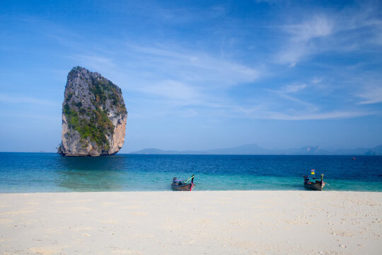 Long tail boats pulled up on shore with a limestone karst in the background.