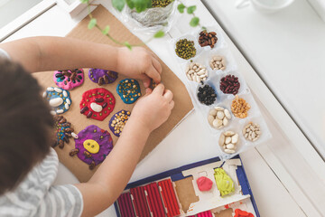 Baby boy creating plasticine diy figure with decorate dried beans element early development top view