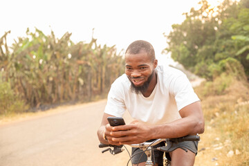 copy space of young black man smiling using phone while sitting on bicycle - obrazy, fototapety, plakaty