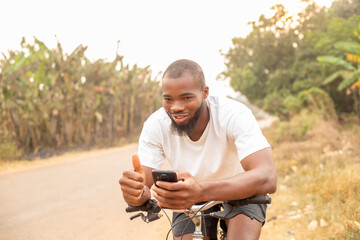 Attractive black model holding mobile while sitting on bicycle making hand gesture