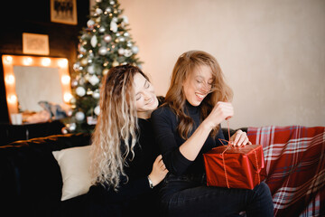 Two beautiful curly girls sisterhood black jackets give gifts on background of Christmas tree,...