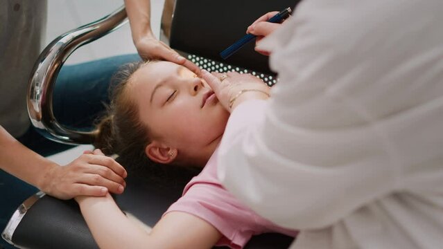 Little kid fainting in hospital waiting area, elderly doctor doing emergency consultation with flashlight. Worried woman supporting girl being sick and unconscious. Handheld shot. Close up.