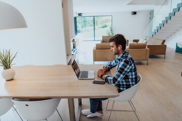 The man sitting at a table in a modern living room, with headphones using a laptop for business video chat, conversation with friends and entertainment