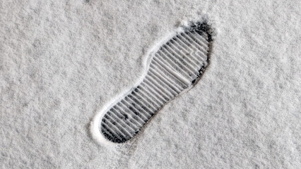 White uneven snow cover. There is a thin layer of freshly fallen snow on the ground. In the snow he sees a clear imprint of the boot of a person who has passed over it. Black asphalt under the snow.