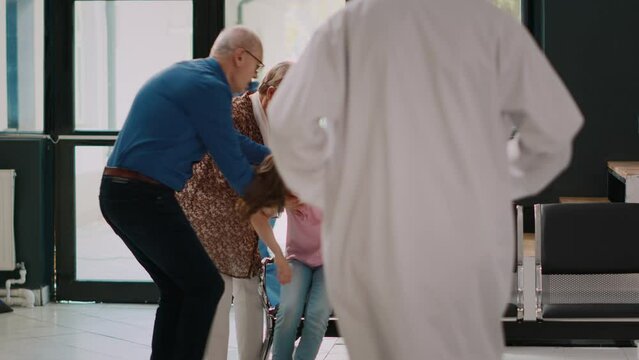 Grandparents taking sick niece to emergency checkup, feeling ill and light headed. Little girl with healthcare problem being unconscious while specialist consults her with flashlight in lobby.