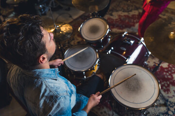 High angle view of male drummer using his wooden sticks. Concert and rehearsal of a garage band. Caucasian man in denim jacket as one of musicians. High quality photo