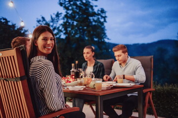 A group of young diverse people having dinner on the terrace of a modern house in the evening. Fun for friends and family. Celebration of holidays, weddings with barbecue.