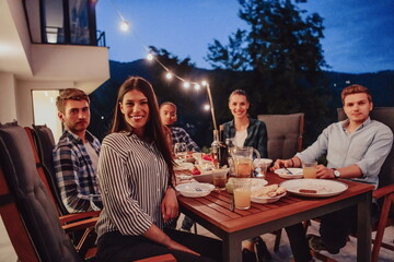 A group of young diverse people having dinner on the terrace of a modern house in the evening. Fun for friends and family. Celebration of holidays, weddings with barbecue.