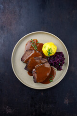 Traditionell geschmorter Sauerbraten vom Rind mit Blaukraut und Kartoffelklößen in würziger...