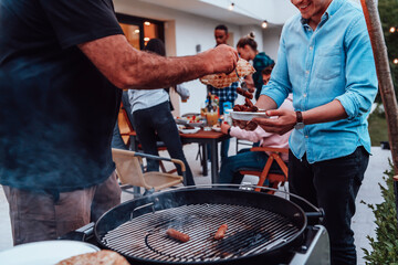 A group of friends and family barbecue together in the evening on the terrace in front of a large modern house