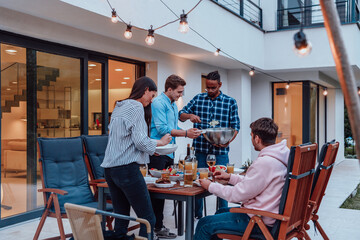 A group of young diverse people having dinner on the terrace of a modern house in the evening. Fun for friends and family. Celebration of holidays, weddings with barbecue.