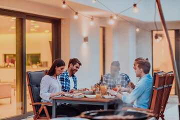 A group of young diverse people having dinner on the terrace of a modern house in the evening. Fun for friends and family. Celebration of holidays, weddings with barbecue.