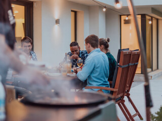 A group of young diverse people having dinner on the terrace of a modern house in the evening. Fun for friends and family. Celebration of holidays, weddings with barbecue.