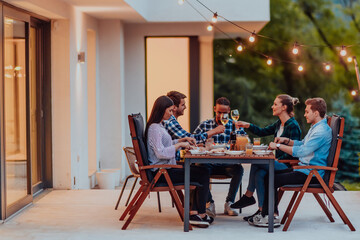 A group of young diverse people having dinner on the terrace of a modern house in the evening. Fun for friends and family. Celebration of holidays, weddings with barbecue.