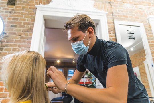 Male hairdresser in protective mask cutting hair of a woman with scissors. High quality photo