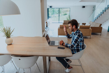 The man sitting at a table in a modern living room, with headphones using a laptop for business video chat, conversation with friends and entertainment