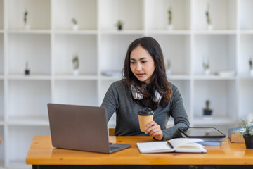 Young adult happy smiling Hispanic Asian student wearing headphones talking on online chat meeting using laptop in university campus or at virtual office. College female student learning remotely.
