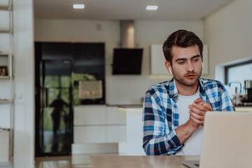 Fototapeta premium The man sitting at a table in a modern living room, with headphones using a laptop for business video chat, conversation with friends and entertainment