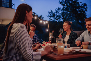 A group of young diverse people having dinner on the terrace of a modern house in the evening. Fun for friends and family. Celebration of holidays, weddings with barbecue.