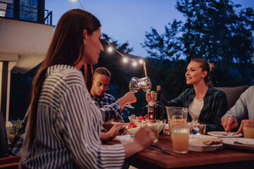 A group of young diverse people having dinner on the terrace of a modern house in the evening. Fun for friends and family. Celebration of holidays, weddings with barbecue.