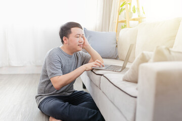 Fototapeta premium Asian man sitting on floor and do work with laptop computer, he work from home and search information, internet and network technology
