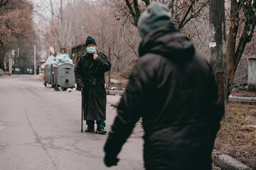 An elderly man with a cane wearing a medical mask and a long black jacket walk along the street. Old man. senior. Pollution. Standing. Stroke. Protection. Coronavirus. Disabled. Movement. Prevention