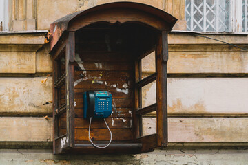 Old wooden empty public telephone booth mounted on the facade of the building. Electronic. Calling....