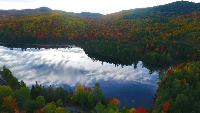 Aerial pan over morning light shining over reflective lake and stunning mountains of peak fall foliage