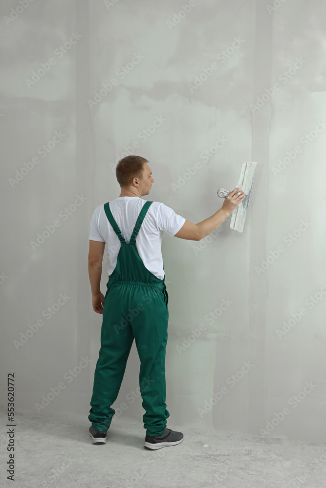 Wall mural Professional worker plastering wall with putty knife indoors