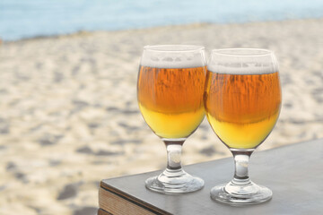 Glasses of cold beer on table near sea, space for text