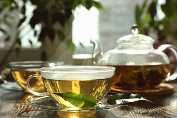 Fresh green tea in glass cups, leaves and teapot on wooden table