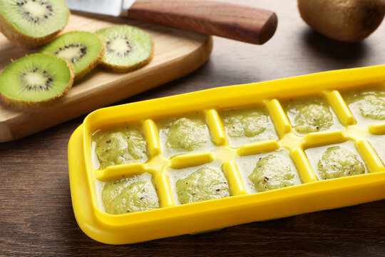 Kiwi puree in ice cube tray and ingredients on wooden table. Ready for freezing