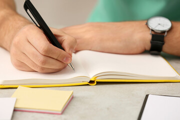 Man writing in notebook at table indoors, closeup