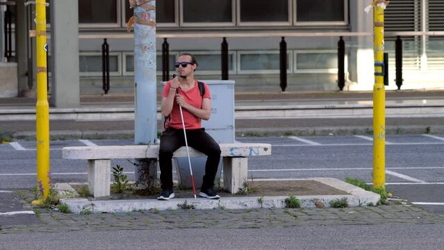 blind man sitting on a bench undecided whether to cross the road