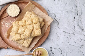 Wooden tray with delicious sweet kozinaki bars, sesame seeds and honey on white textured table,...