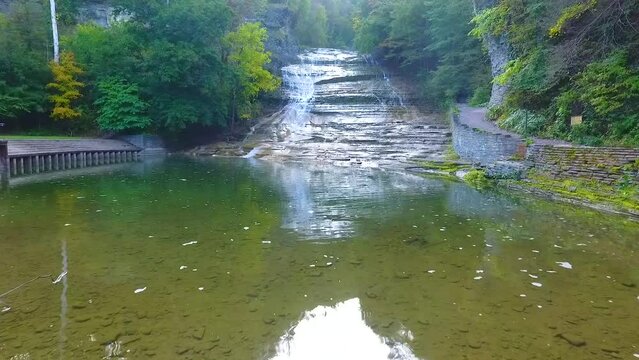 Aerial over hiking bridge viewing huge cascading waterfall over rocks in forest park of New York