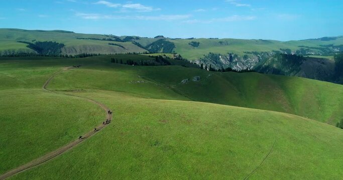 aerial landscape of Beautiful Xinjiang Nalati grassland scenery under the blue sky, small group of tourist riding on the horse travel on the plateau