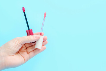 Female hand holds lipstick brushes close-up on blue background copy space.