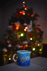 blue cup with hot on the background of a christmas tree with lights in the bokeh - 553626505