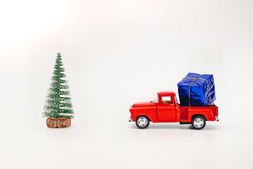 toy red truck carries a gift under the Christmas tree on a white background, copy space - 553626547