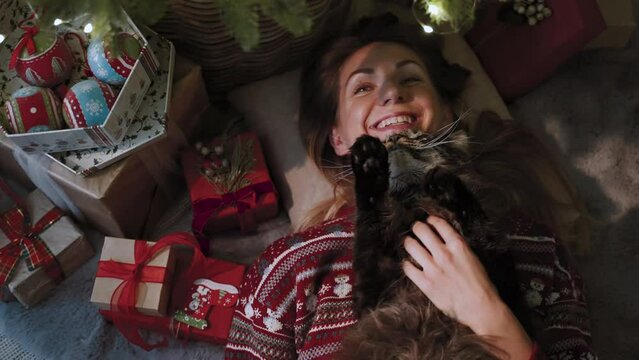 A beautiful woman, in the company of her favorite cat, lies under a Christmas tree with a lot of presents. New year celebration concept.